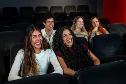 Friends laughing and enjoying a comedy movie at the cinema, sharing joyful moments together in a