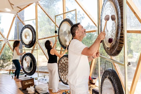 Sound therapists perform a gong bath, creating soothing vibrations with various gongs. The serene