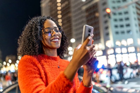Smiling woman browsing social media on mobile phone in urban environment with bokeh lights