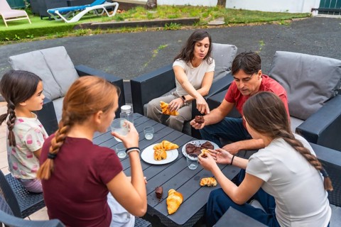 Family gathered around a patio table enjoying pastries and drinks, sharing relaxed conversation and