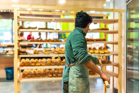 Rear view of a latin man placing baked artisan bread to shelf in the bakery shop