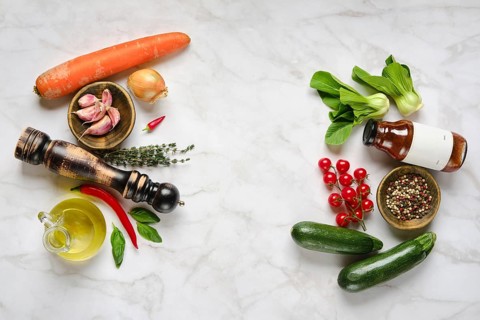 A variety of fresh vegetables, herbs, and condiments are beautifully arranged on a marble