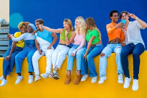 Young multi-ethnic friends taking selfies sitting outdoors on a colorful urban wall