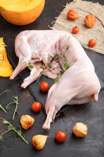 Whole raw rabbit with pumpkin, tomatoes, pea sprouts on a black concrete background and linen