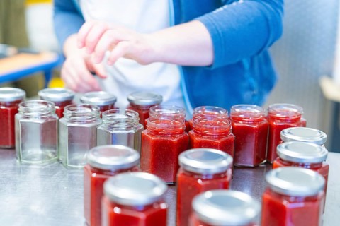 Person working with jars, some are unfilled, others are filled with red jam, jam production,