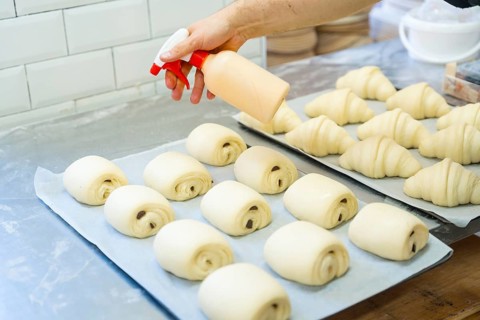 Baker of bakery in the workshop workshop of artisan bakery preparing croissant for baking with a