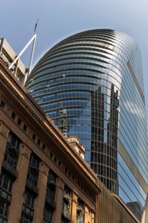 A sleek, modern skyscraper with a glass facade reflects the sky and surrounding architecture,