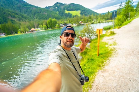 Tourist taking a selfie at lake dobbiaco, surrounded by breathtaking mountains, enjoying summer
