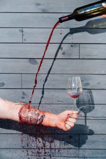 A visually striking composition of red wine being poured into a glass through a tattooed arm,
