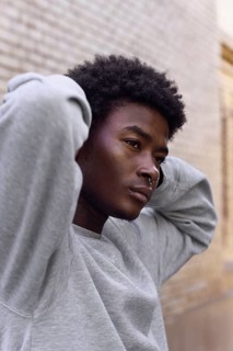 Portrait of a young black man with a reflective gaze, looking away while standing outdoors, dressed