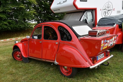A red Citroën 2CV is parked next to a motorhome with lots of stickers, vintage Citroën 2CV6 at a