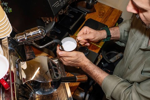 A barista froths milk for a specialty coffee using a professional espresso machine. This process