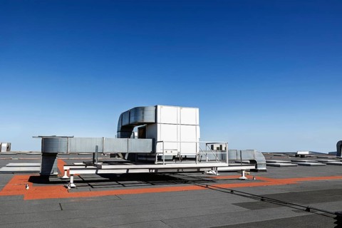 A rooftop industrial air conditioning unit stands out against a clear blue sky, showcasing robust