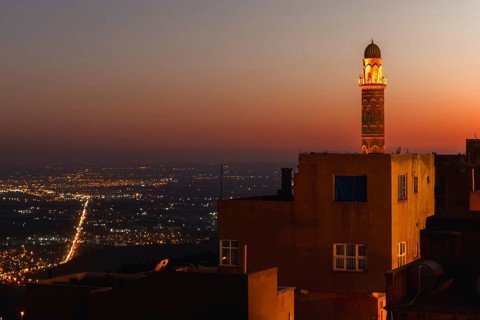 Illuminated mosque minaret above Mardin old town with glowing city lights and Mesopotamian plains