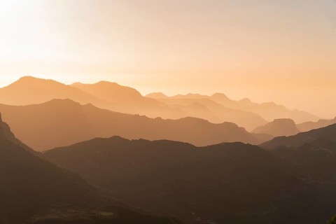Golden sunset casting a soft glow over the layered mountain ranges seen from the viewpoint near