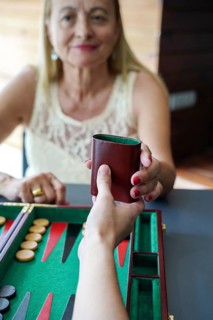 Close-up of two people playing backgammon One hands a dice cup to the other, while game pieces rest