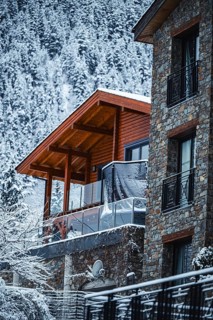 A wooden cabin with stone accents nestled in a snowy mountain landscape of Andorra. The serene