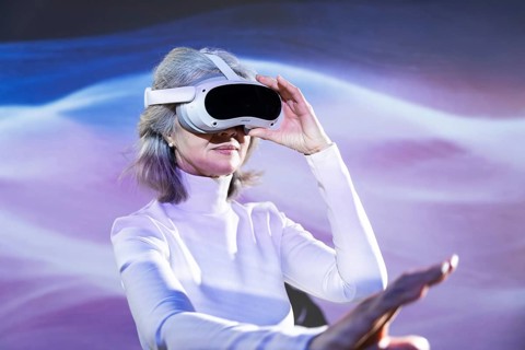 An elderly Asian woman wearing a VR headset explores the vibrant metaverse. Her advanced age