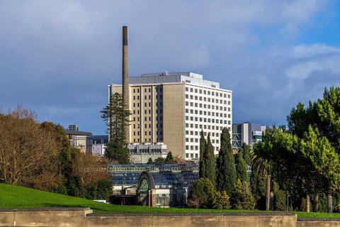 Auckland City Hospital tower block with tall brick chimney rising above glasshouse rooftop,