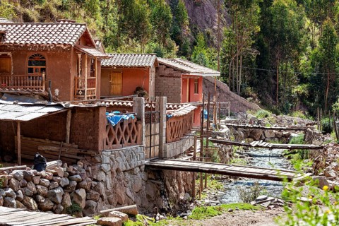 Rustic clay houses near a wooden bridge over a small river in rural surroundings, village with