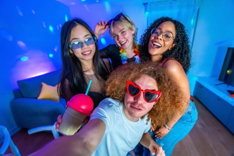Cheerful multi ethnic friends enjoying a vibrant home disco party, posing for a selfie with