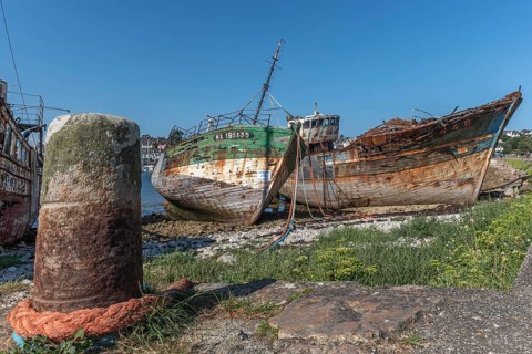 A rustic boat lies on the shore next to a large concrete pier. The boat is old and has been