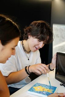 Two smiling teenagers, a non-binary individual and a female, joyfully engage in a creative painting