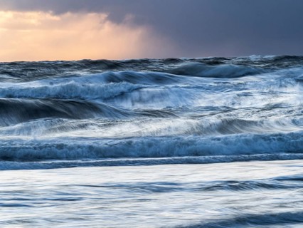 Stormy North Sea and sky with large waves breaking on to the beach, in late evening light, island