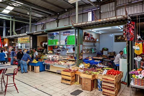 Covered market area with boxes full of fruit and meat products, bustling atmosphere, The Calama