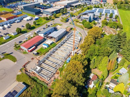 Aerial view of a construction site with a crane in the midst of urban buildings and green spaces,