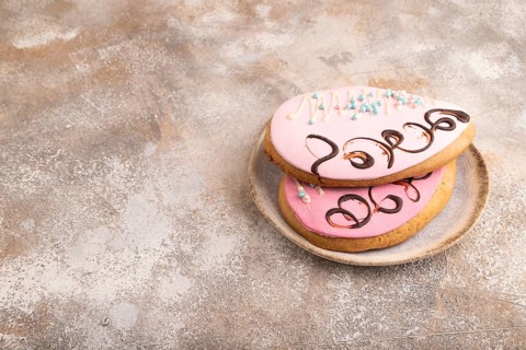 Glazed pink and blue decorated cookies, on brown concrete background, copy space, side view