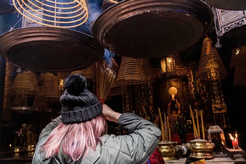 Back view of unrecognizable woman with pink hair lights incense sticks beneath hanging spiral