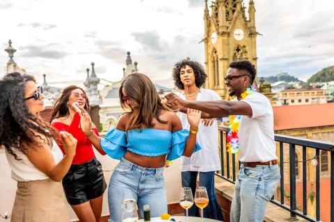 Latin woman dancing with multi-ethnic friends during rooftop party during sunset in the city
