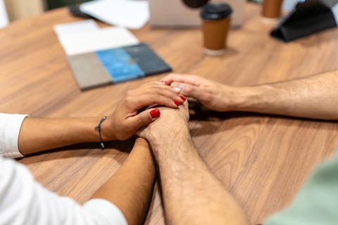 Diverse couple's hands clasped together, showing empathy, unity, and love during a discussion about