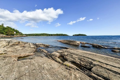 Clear sky over rocky archipelago coastline with granite archipelago with green forest and blue