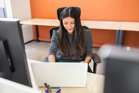 A professional woman is concentrating on her laptop while seated at a modern office desk,