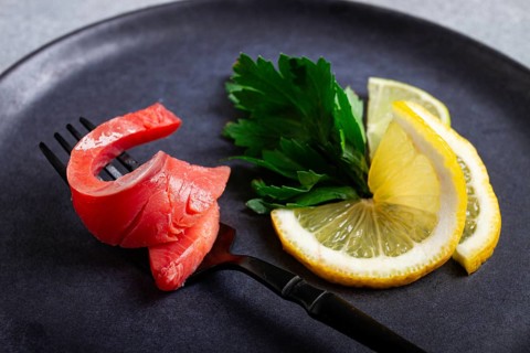 Chum salmon, cold smoked, on a fork, with lemon and parsley, top view, close-up, no people