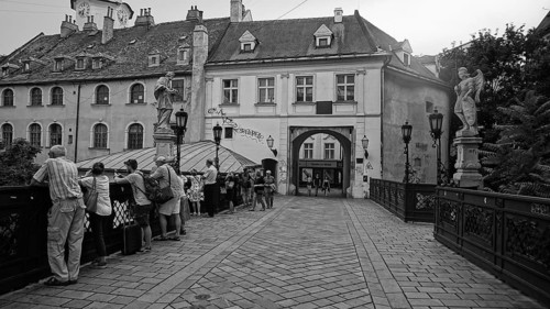 Tourists explore a historic bridge with statues in an urban setting, monochrome, Bratislava