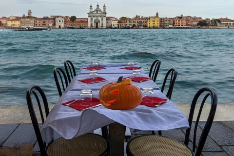 Halloween pumpkin on a set restaurant table on the shore in windy weather, Guidecca, back Venice,