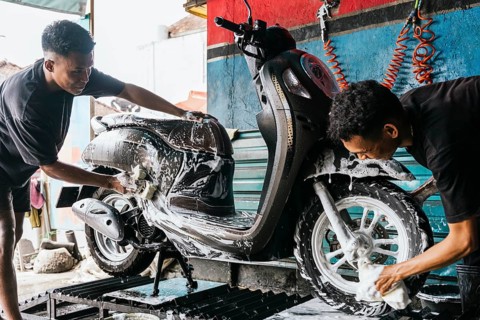 Two asian men meticulously wash a motorcycle, surrounded by soap suds and water. The scene captures