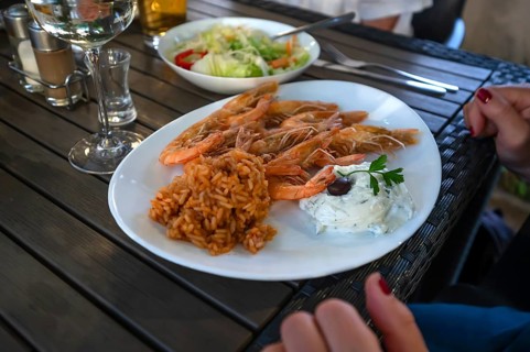Grilled prawns served with red rice and creamy tzatziki with an olive, served in a Greek garden