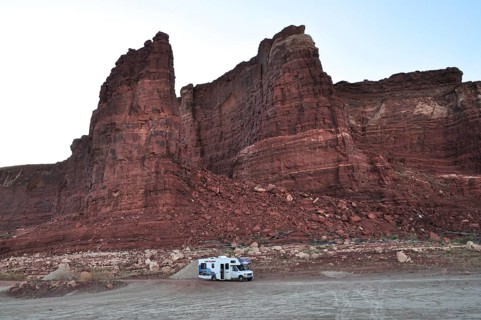 An RV stands in front of massive red rocks in a tranquil desert atmosphere, Lake Powell, Arizona,