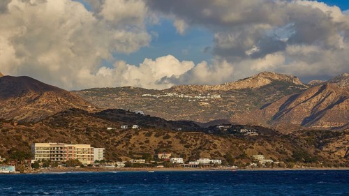 Coastal landscape with mountains, cloudy sky and buildings in the background, hotels, Pigadia, town