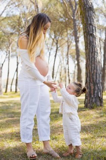 A serene moment between a pregnant woman and her daughter in a lush forest. The child joyfully