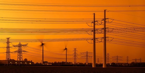 High-voltage electricity pylons, transmission towers and wind turbines at sunset near the Borssele