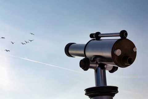 Telescope pointing to blue sky with flock of birds, symbolic image hobby birdwatching, nature