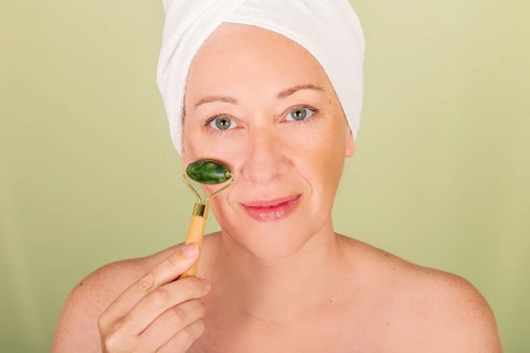 A woman with a towel wrapped around her head uses a jade roller on her face, symbolizing relaxation