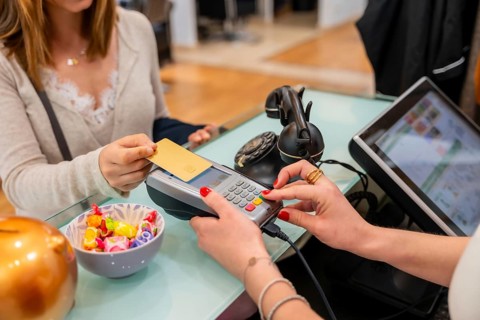 Customer completing a transaction by tapping a credit card on a payment terminal, while a cashier