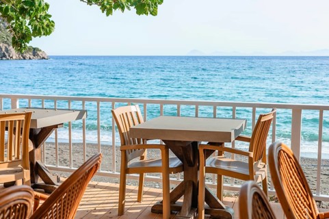 Brightly lit seaside dining space features wooden tables and chairs with stunning ocean views,