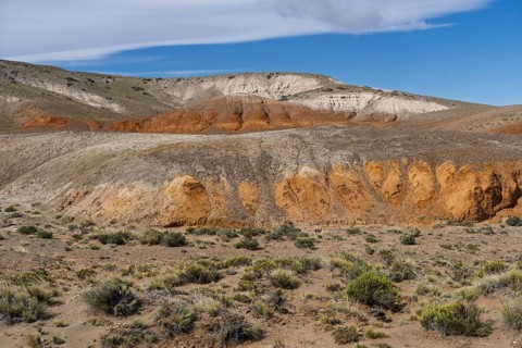 Colored sediment layers in arid hills, badlands with red-orange and white erosion formations,